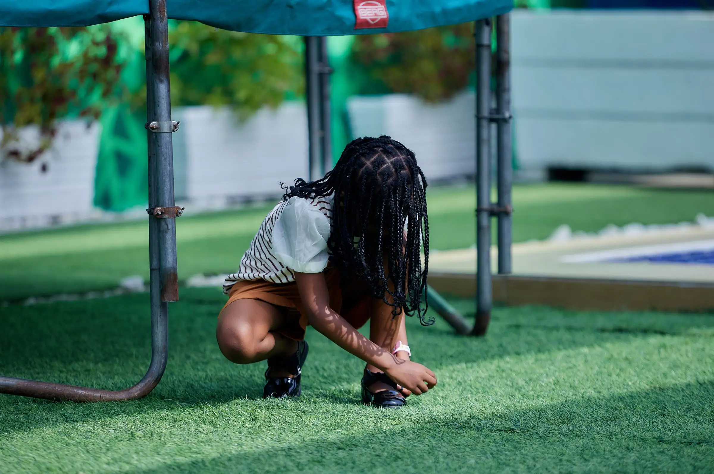 Child crouching on artificial turf under a trampoline