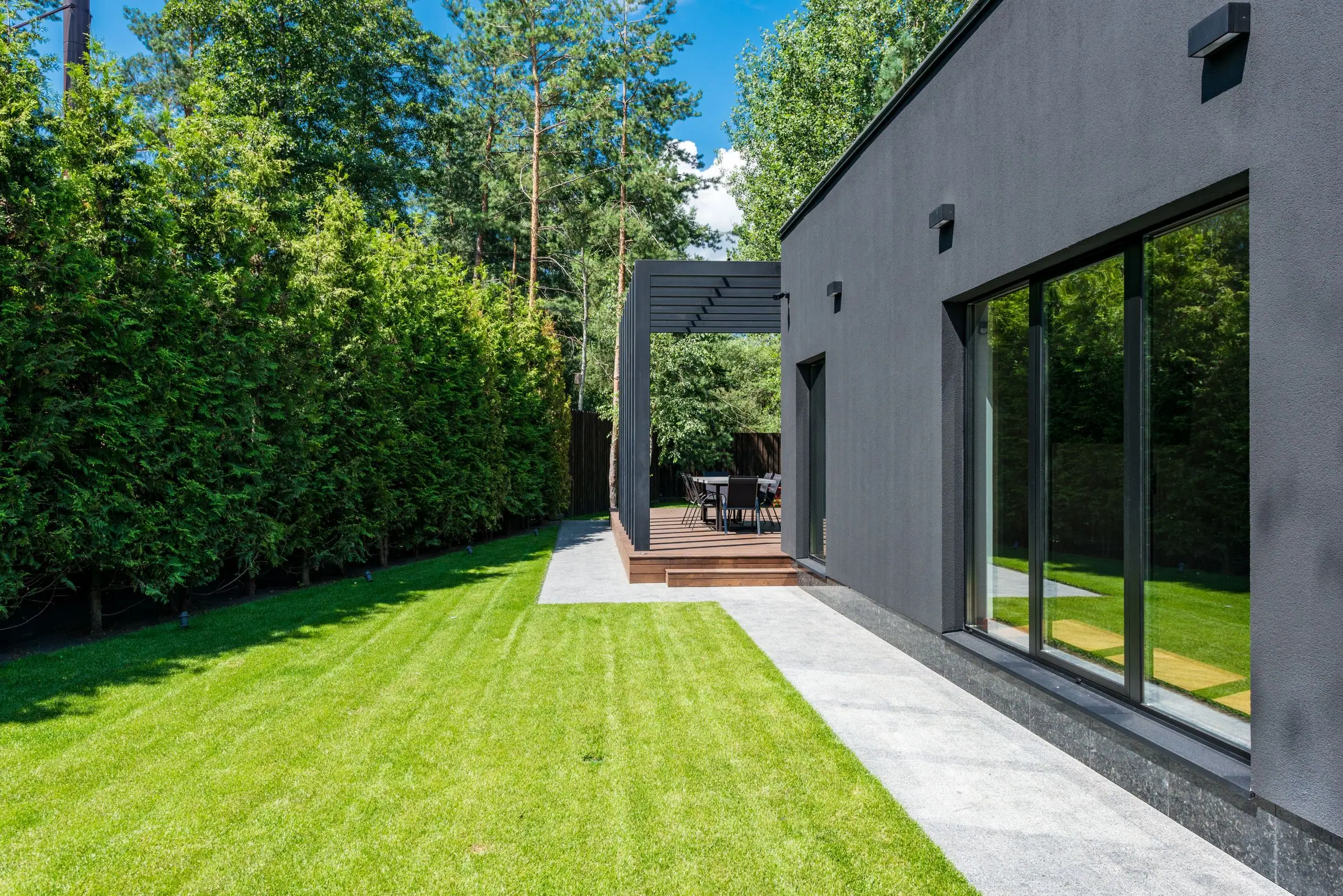 Narrow modern backyard with a green lawn and a stone walkway