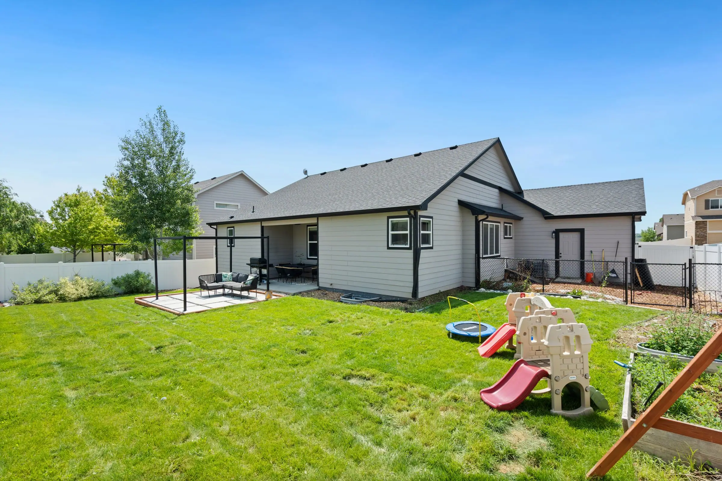 Backyard lawn with a small slide and play set beside a covered patio