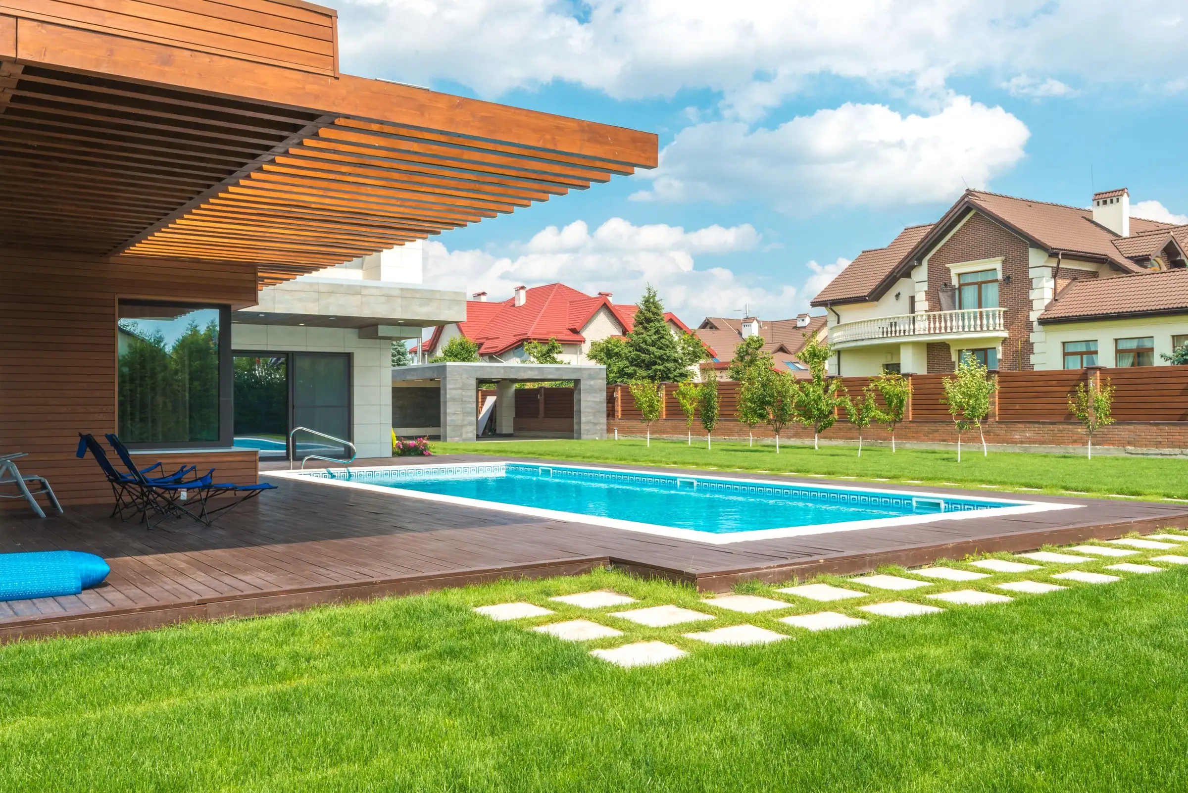 Modern home with a pool, lounge deck and green lawn under clouds